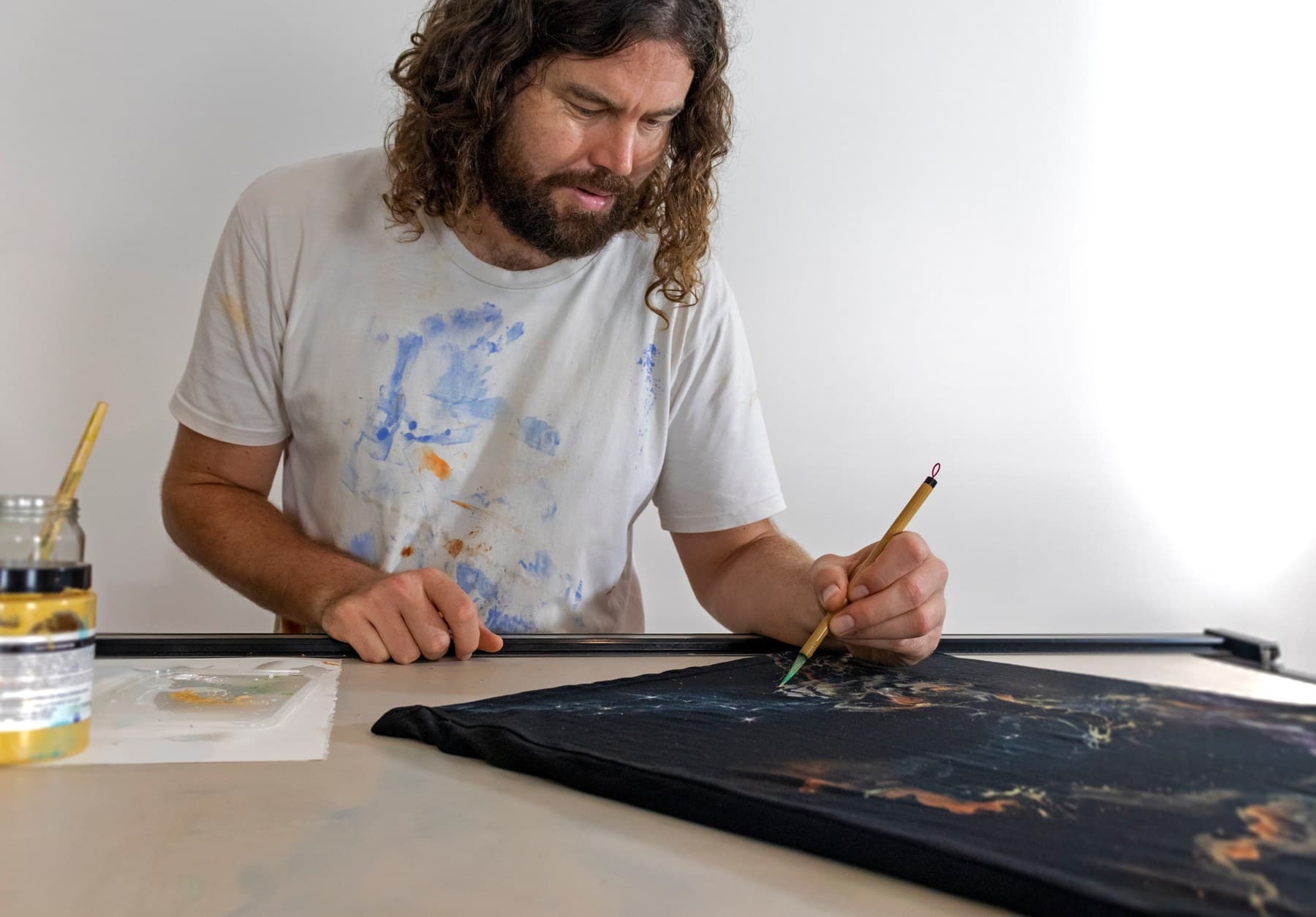 Sebastian painting a Galaxy shirt stretched across a studio table.