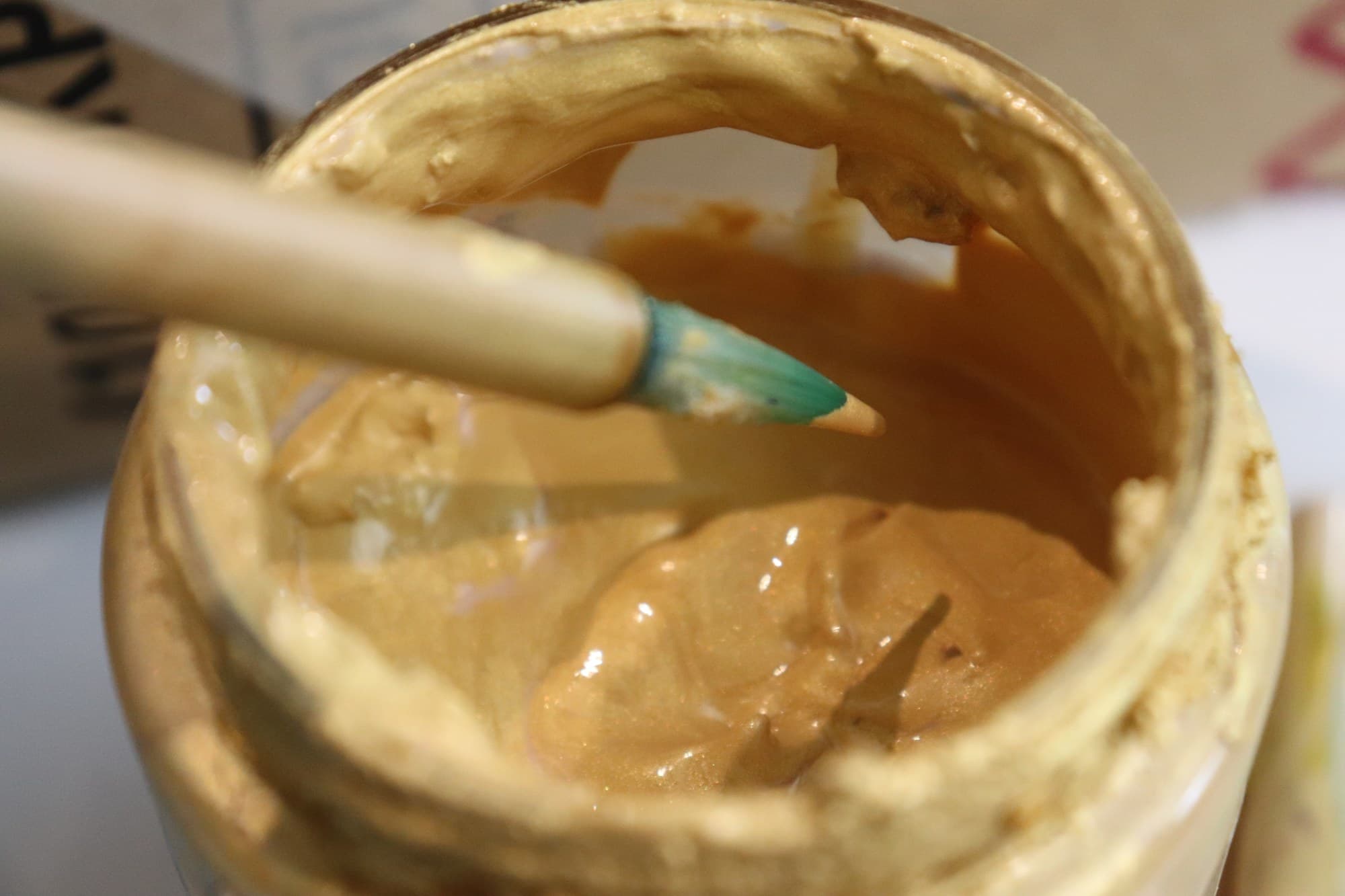 A brush resting in an open pot of gold paint.