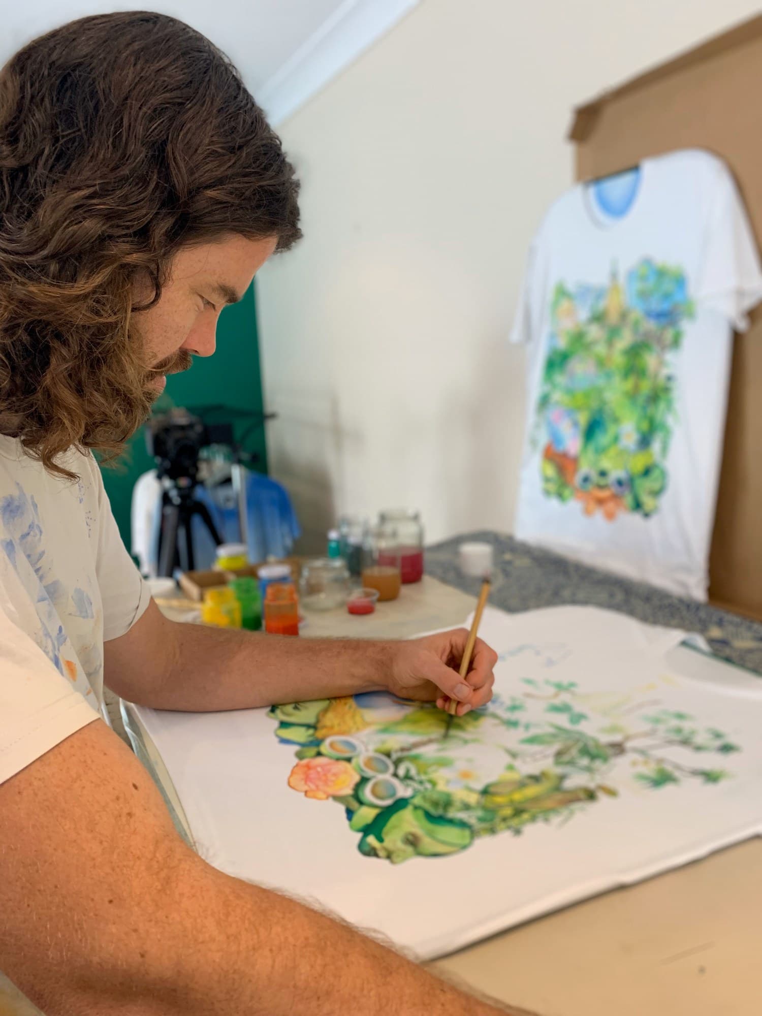 Sebastian leaning over the table to paint a Jungle shirt.