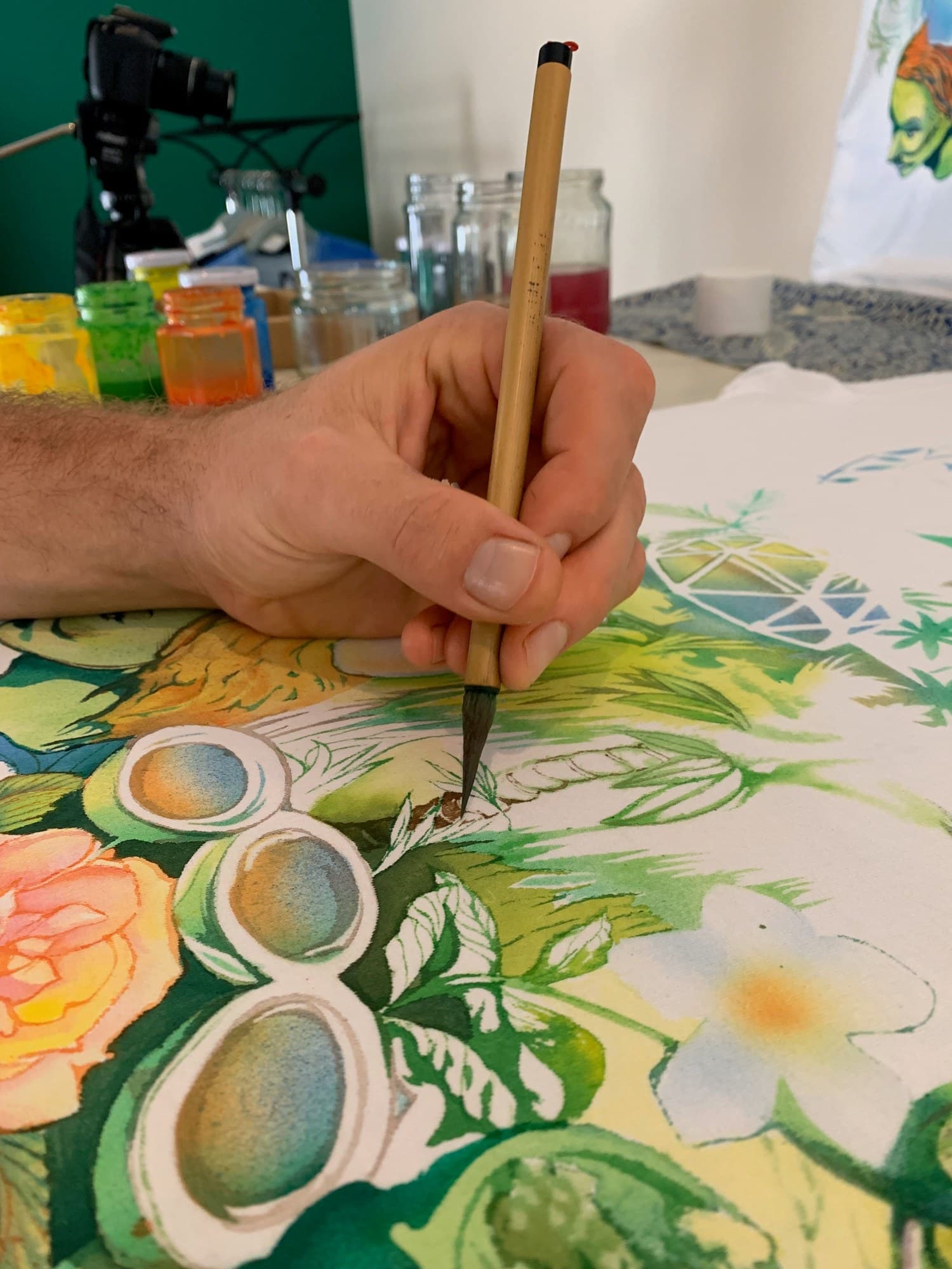 A fine brush working on colourful rounded details in a Jungle shirt painting.