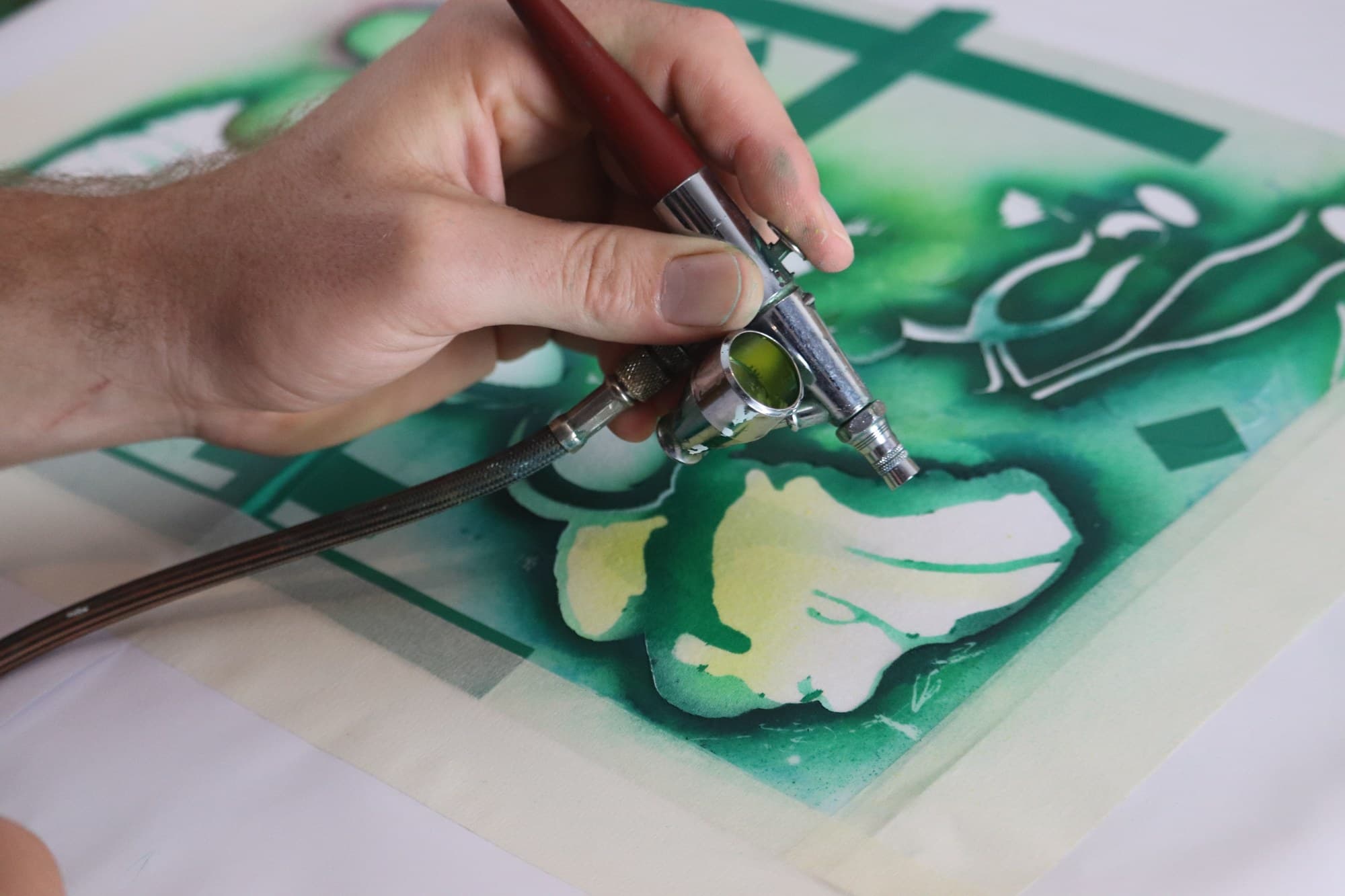 A small brush applying paint through a green stencil.