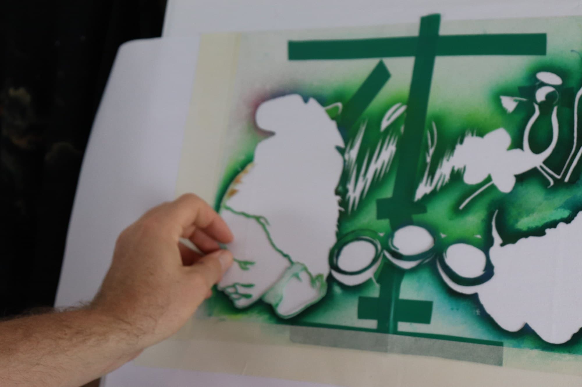 A hand holding a green stencil over fabric on the painting table.